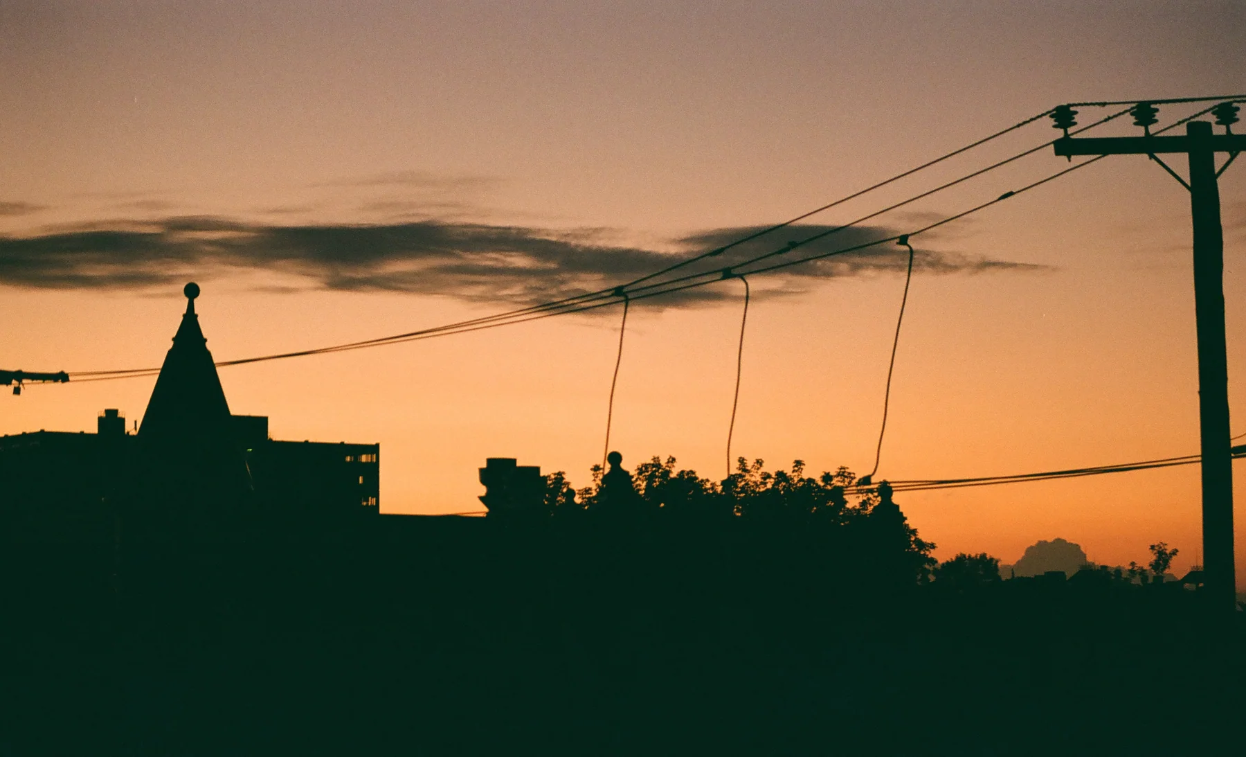 Rooftops and utility lines silhouetted against an orange sky