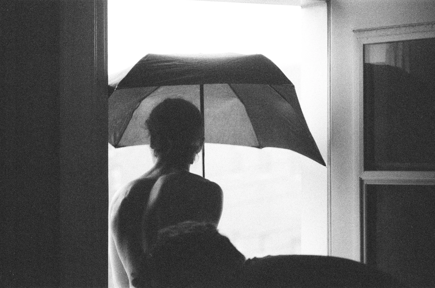 A silhouetted figure holding an umbrella in a bright doorway