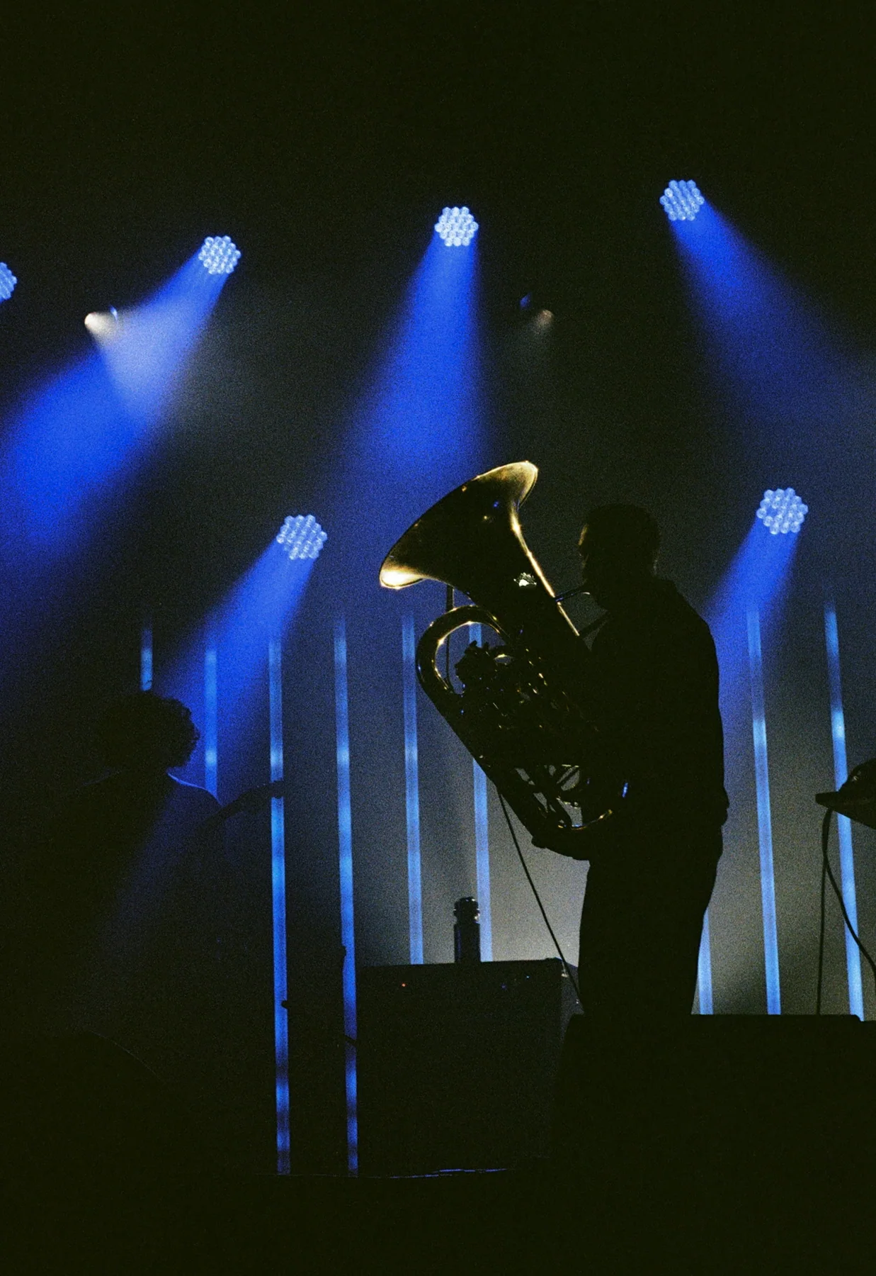 A musician holding a brass instrument beneath blue stage lights