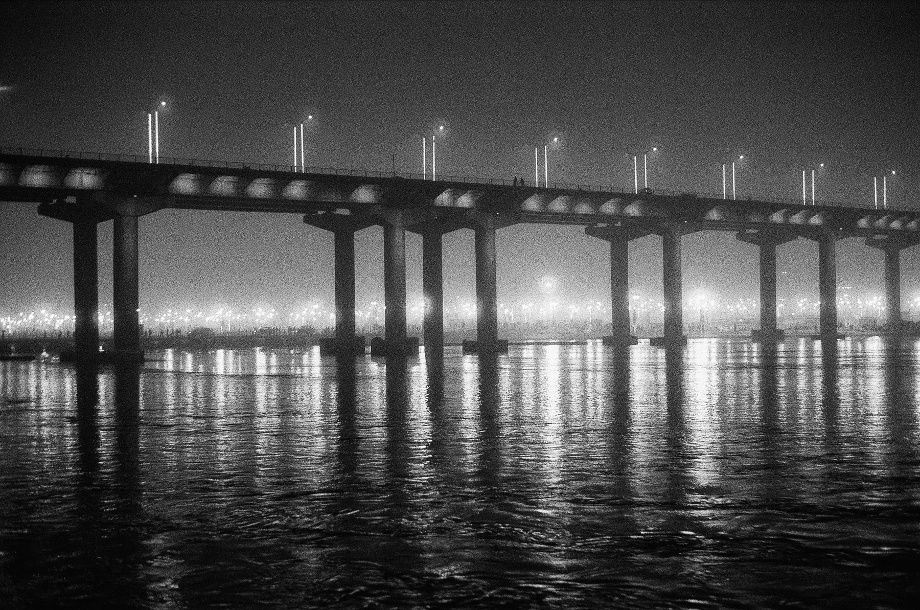 A lit bridge reflected in dark water at night